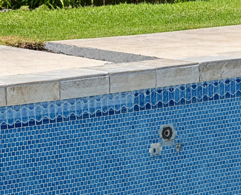 Dark and white buildup along blue swimming pool waterline tiles in a tropical Oahu setting